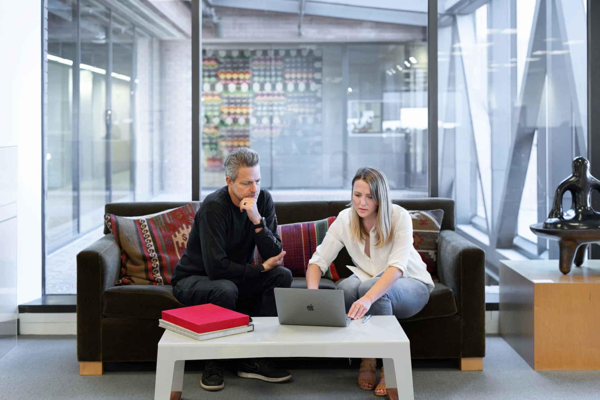 man and woman sitting on couch in an office with a laptop in front of them