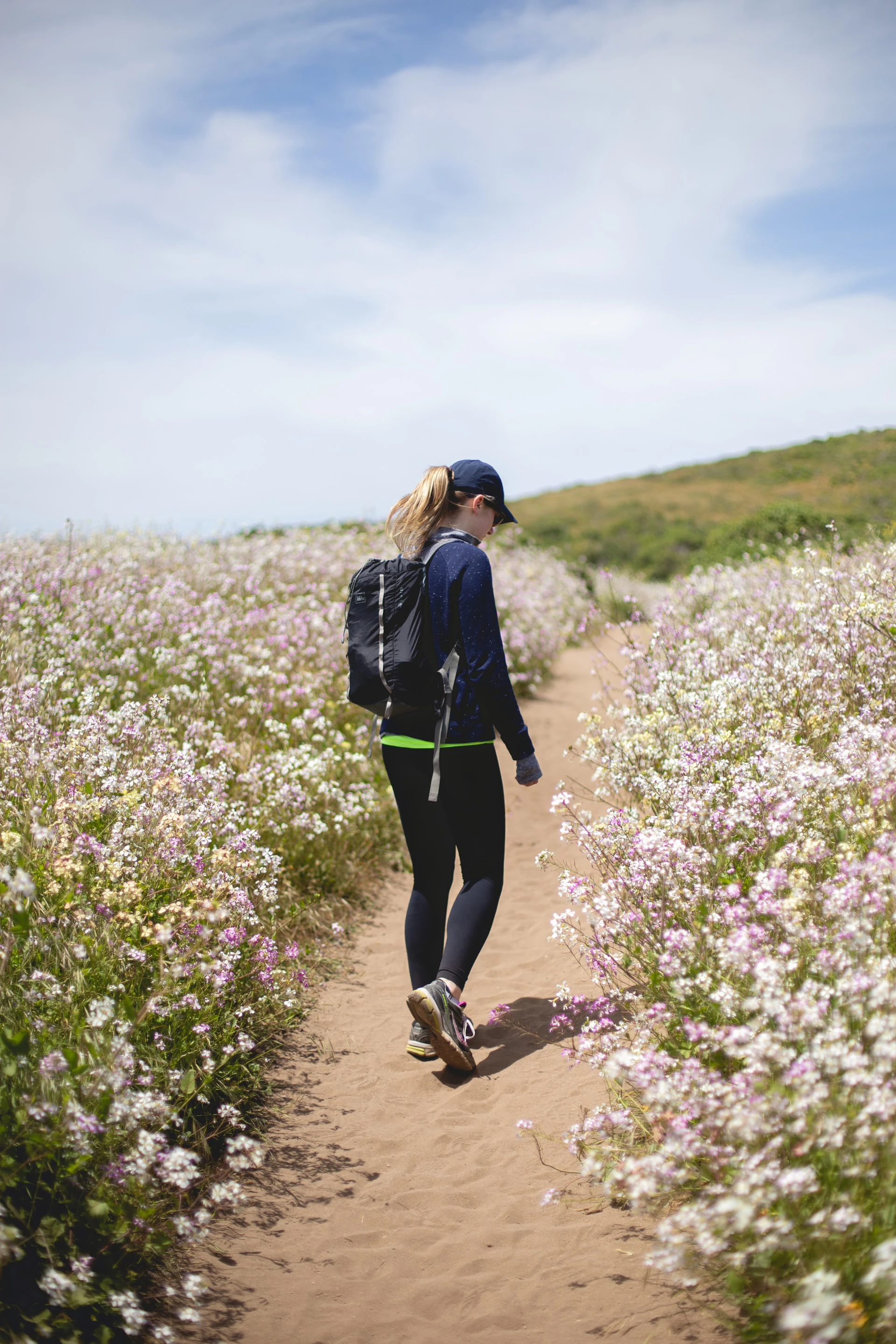 woman wearing dark workout clothes walking on sandy path through flowers